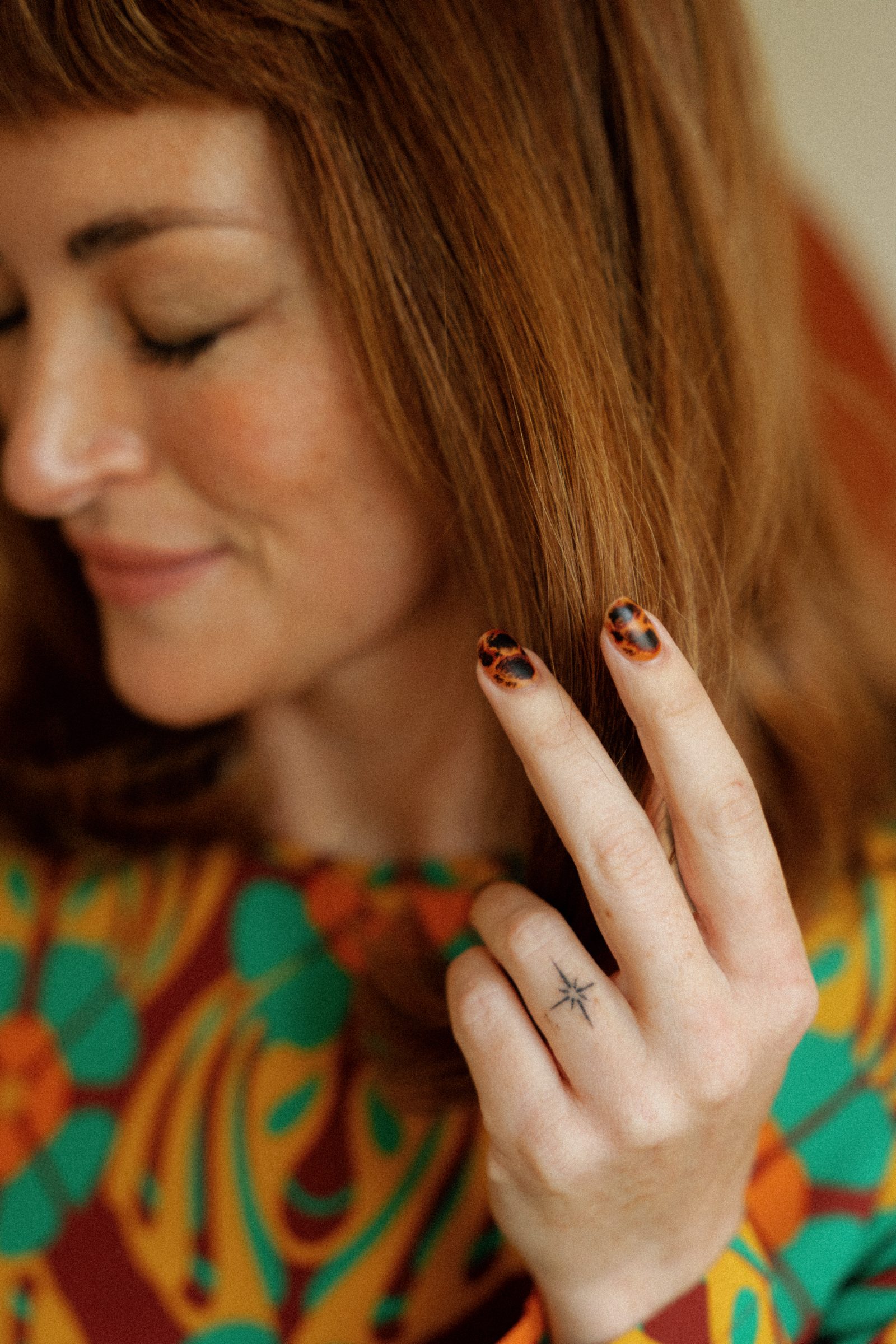 Kira holding a strand of hair, showing tortoise-shell painted nails