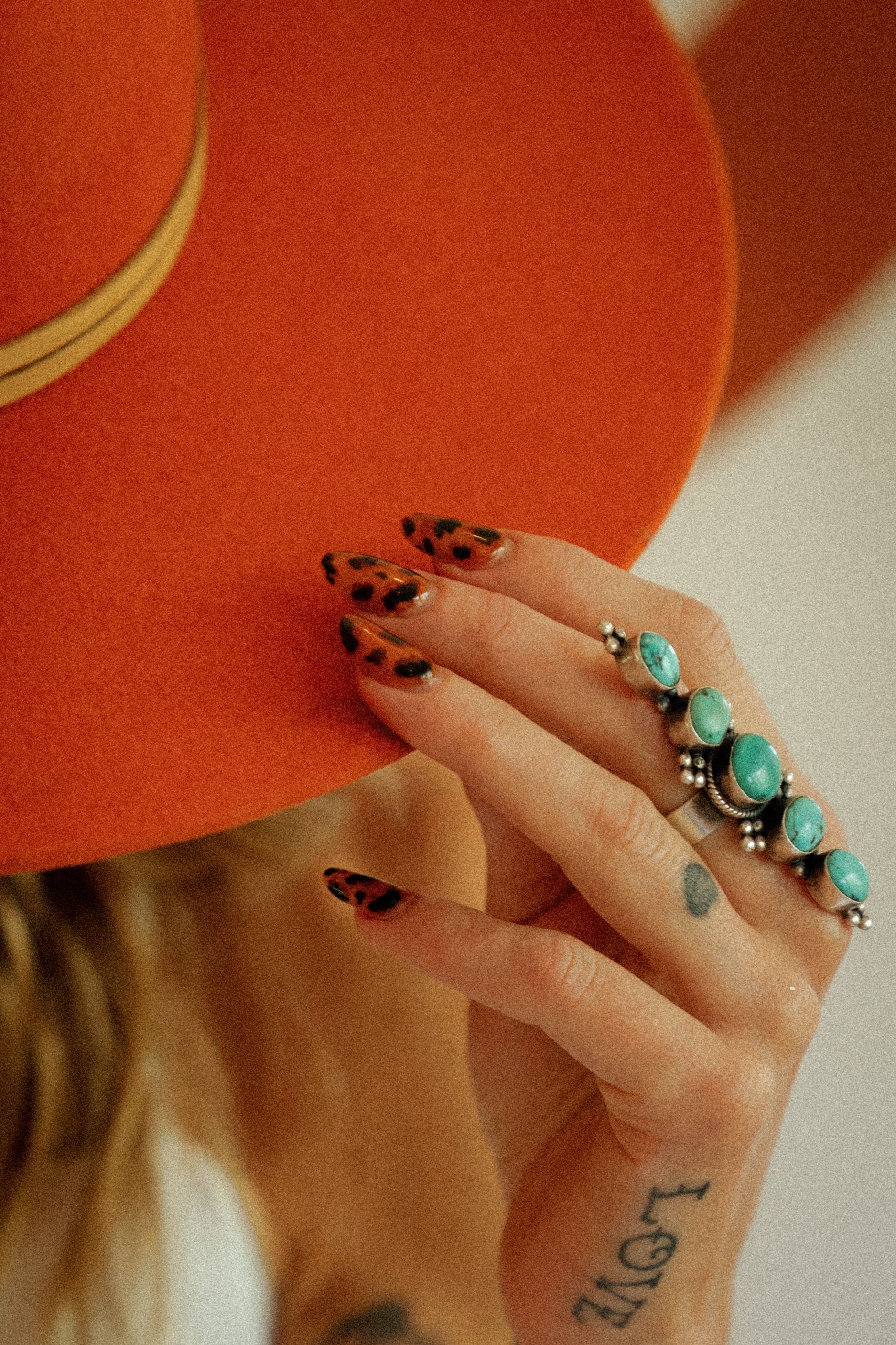 Tortoiseshell almond nails and turquoise rings against a terracotta hat