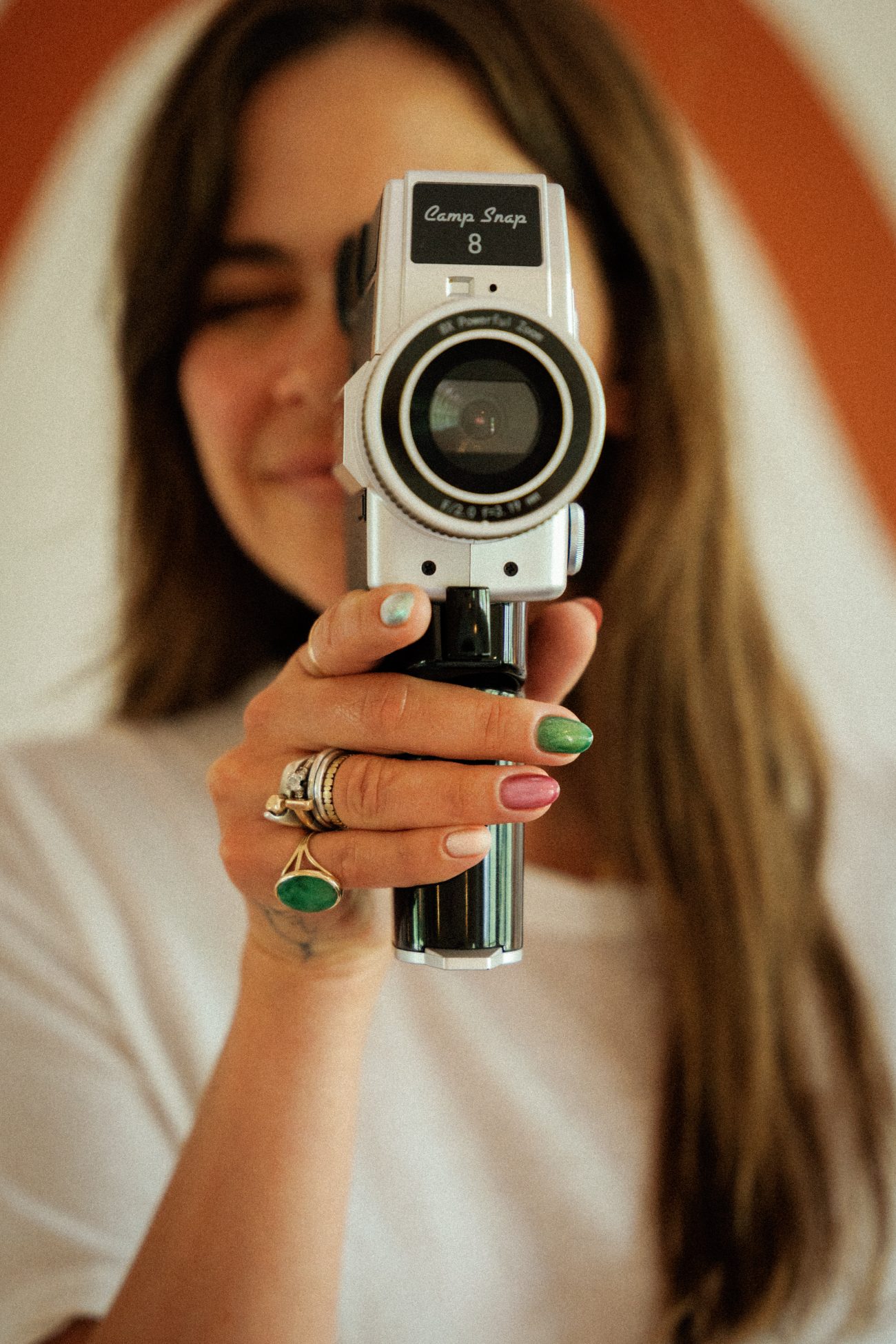 A client with green and pink chrome nails holding a Camp Snap film camera to her eye